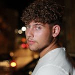 A handsome young man poses on a dimly lit street, creating a captivating night portrait.