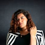 Portrait of a confident woman in a striped jacket against a dark background, showcasing modern style.