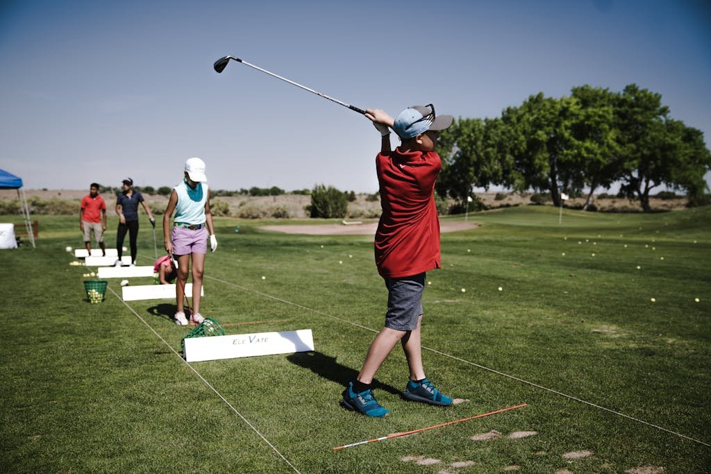 A group of youth practicing golf swings on a sunny day at the driving range.